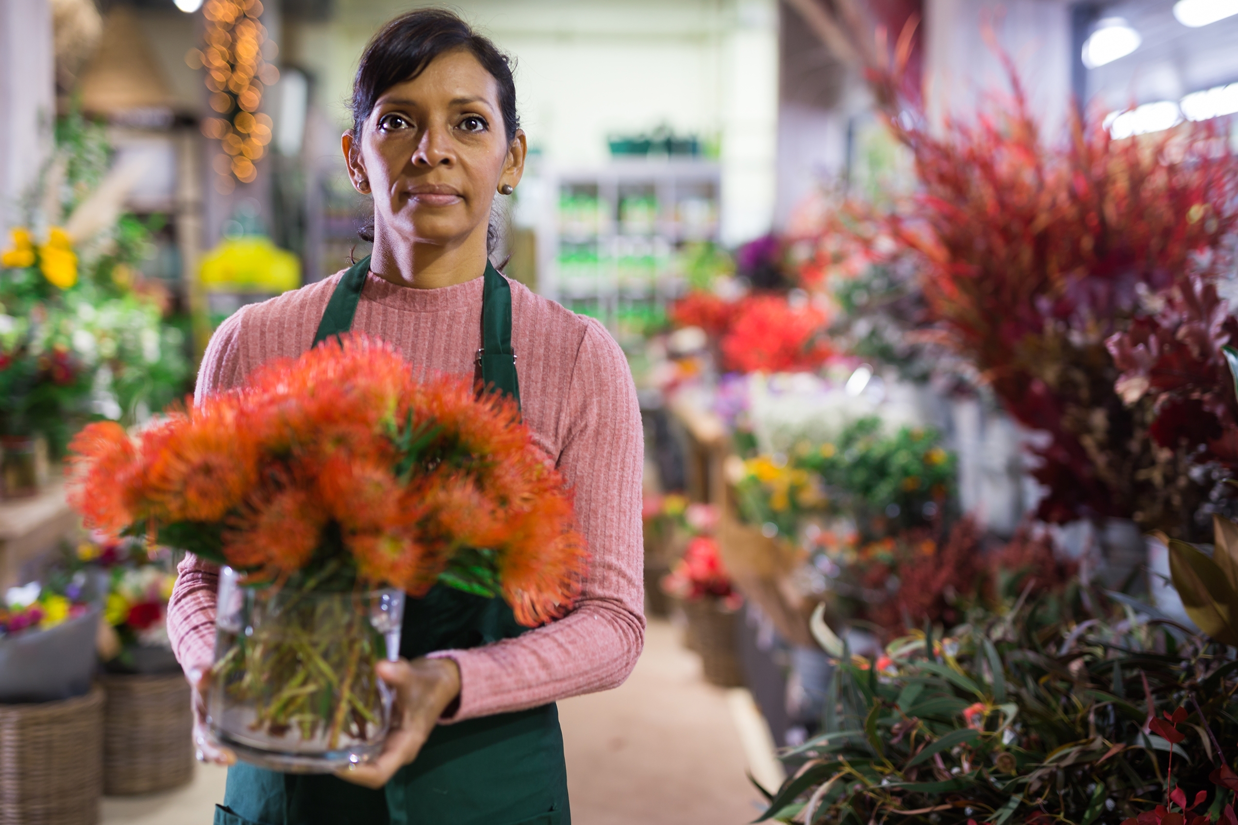Hispanic,Woman,Florist,Carrying,Glass,Vase,With,Orange,Flowers,In